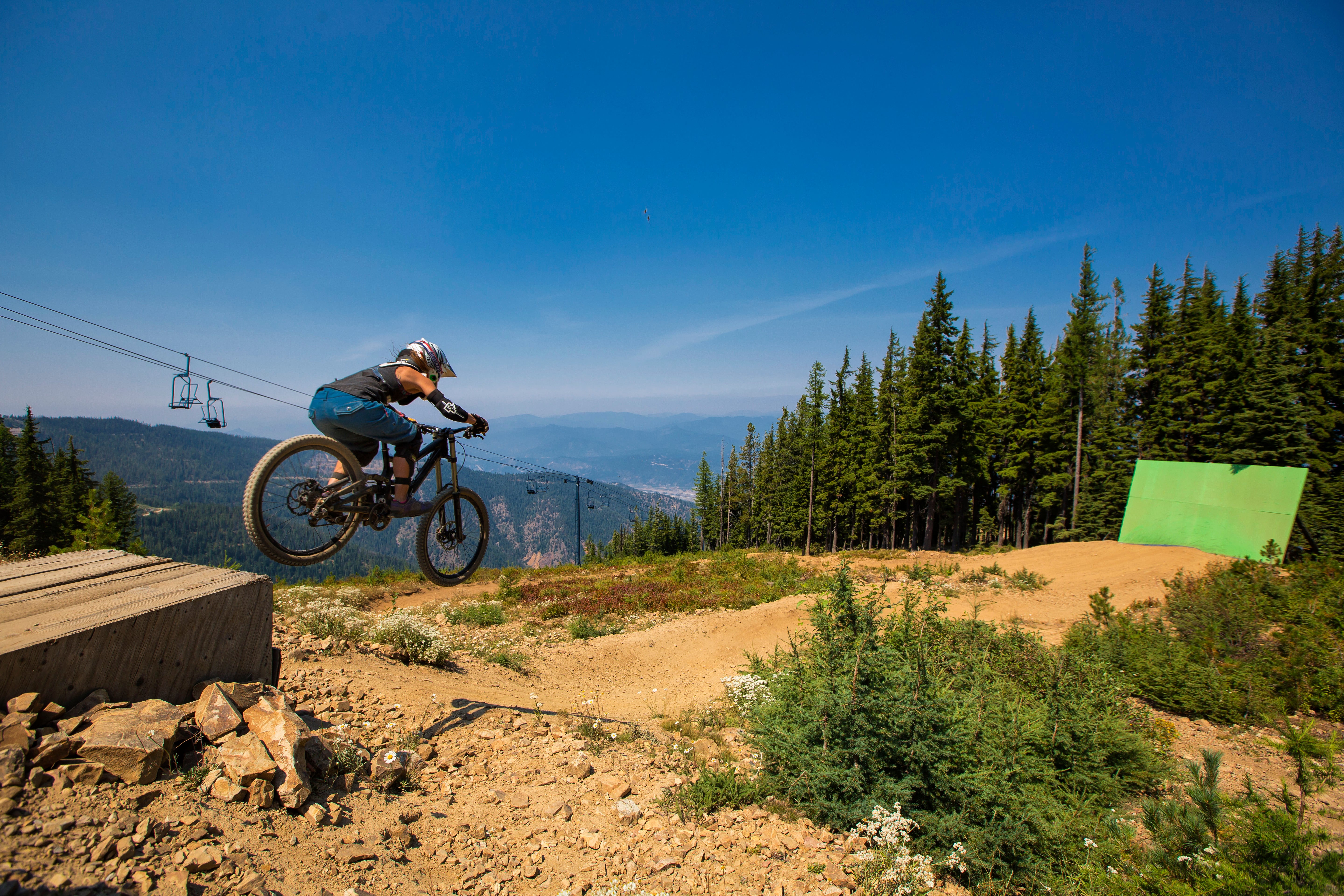 Shan3 Shannon Mahre Skouras sends her mountain bike over a drop on a technical singletrack trail.