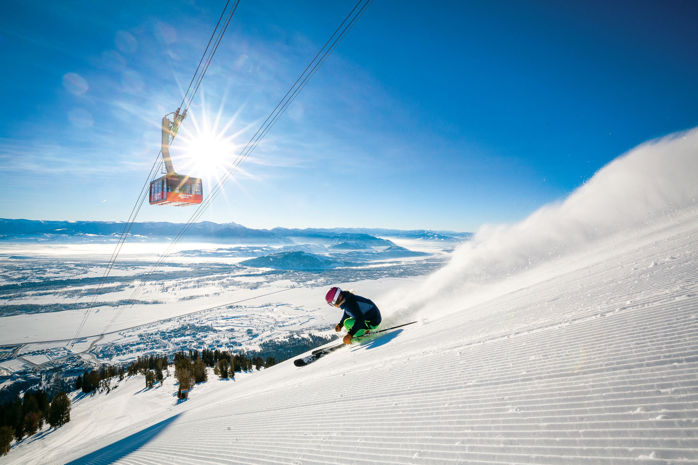 SKI1119-TRA-JHMR-Courtesy1_1 copy Skier skiing down well groomed slope with a gondola above the skier that says Jackson Hole