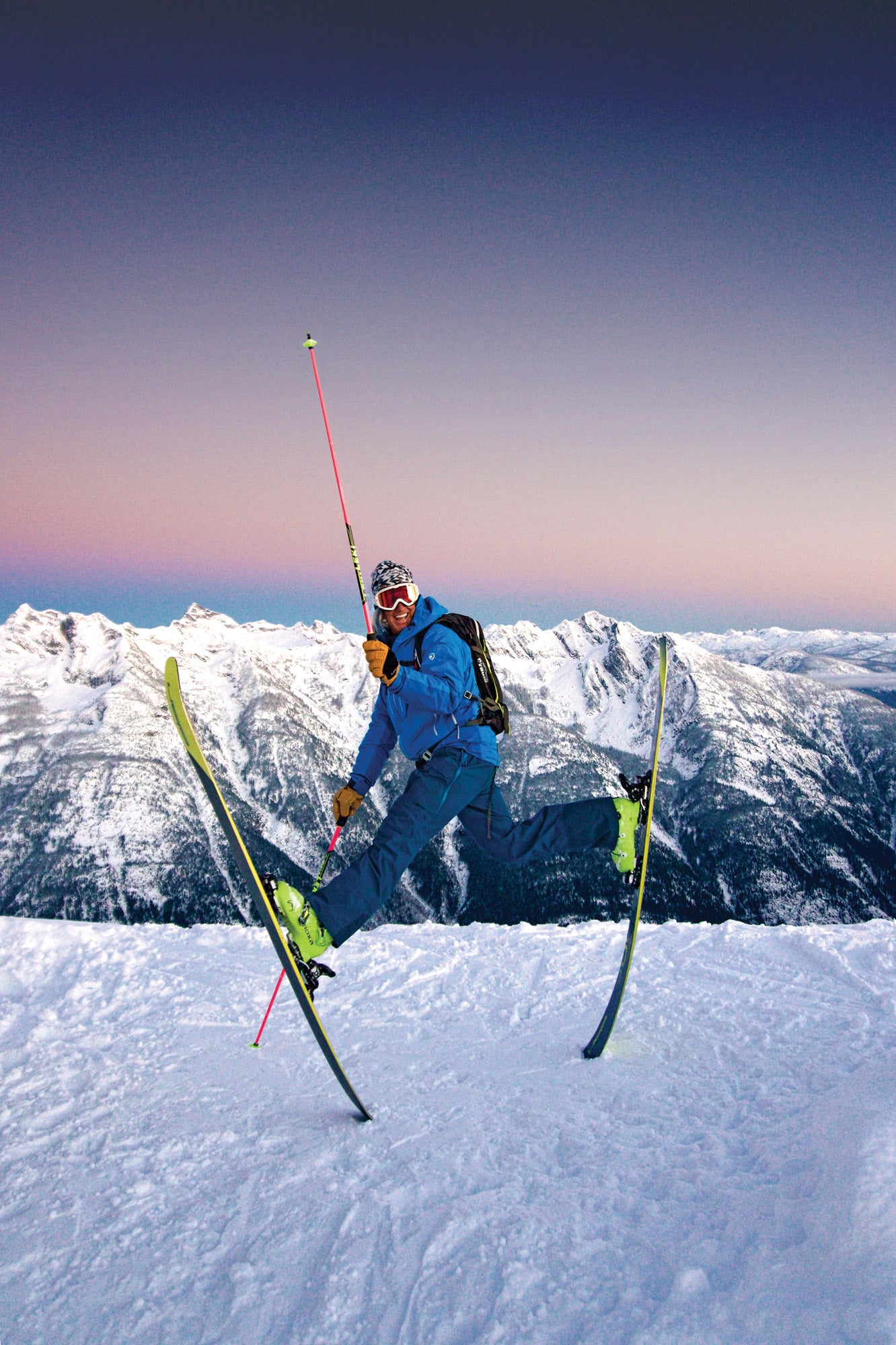 SNW70-Plake1-DannyDeclare copy Skier Glen Pake jumping into the air with his skis on and one pole raised up in front of a snow mountain range