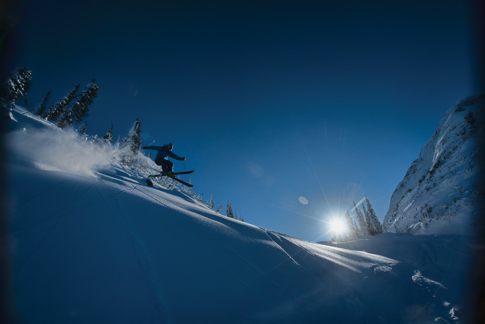 SNW70-Plake2-RyanVarchol copy Skier Glen Plake mid-air while skiing down mountain slope with the sun shadowing him