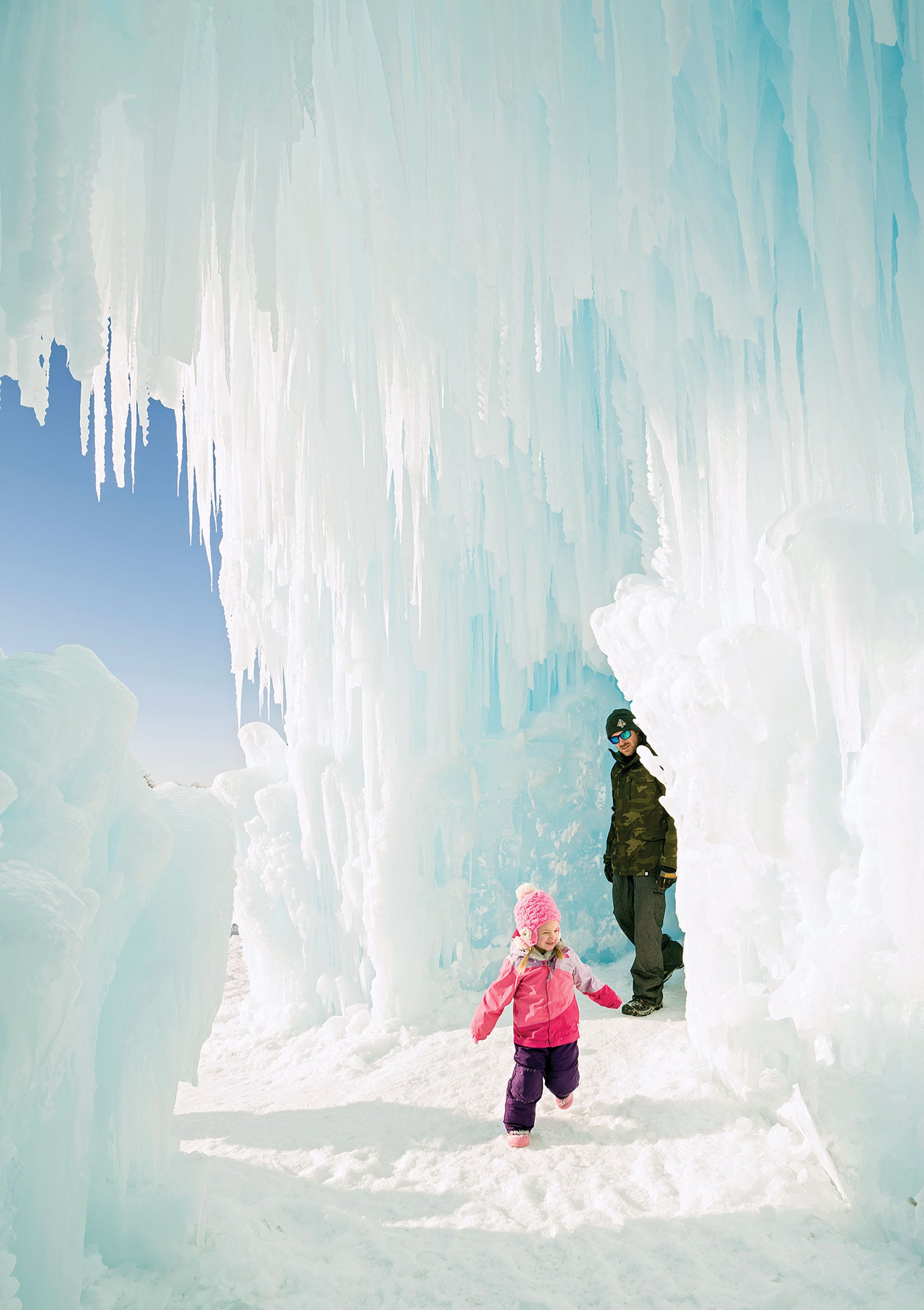 WEB SKI1219-TOW-ParkCityIceCastles-AJ-Mellor-s copy Young girl in pink and purple snow outfit running through midway ice castles with father