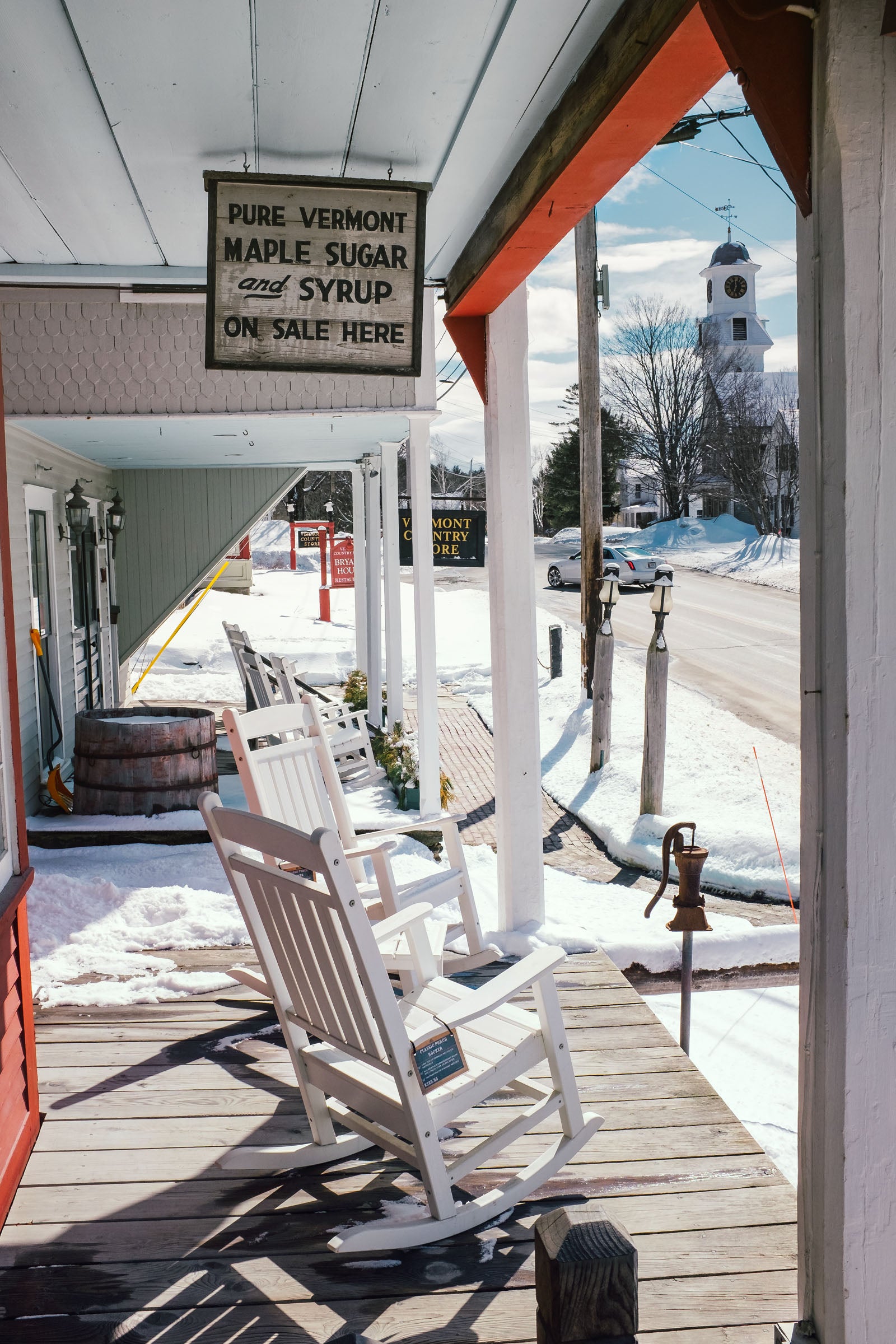 WEB JCash_Stratton_DSF4831_v3 copy Two rocking chairs on a porch in front of a street. The rocking chairs a below a sign that says