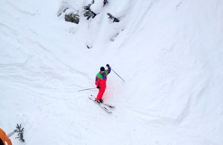 Onesies for Funsies Editor Kevin Luby, formerly clad in canary yellow, rocks a classic Nevica one-piece on day 4 of the Skiing Mag ski test at snowbird, UT. Behind the…