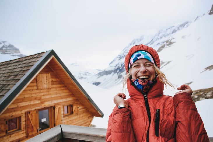_L8A5200-2-1 (1) Corinne Prevot laughing in orange snow coat in front of ski cabin in the French Alps