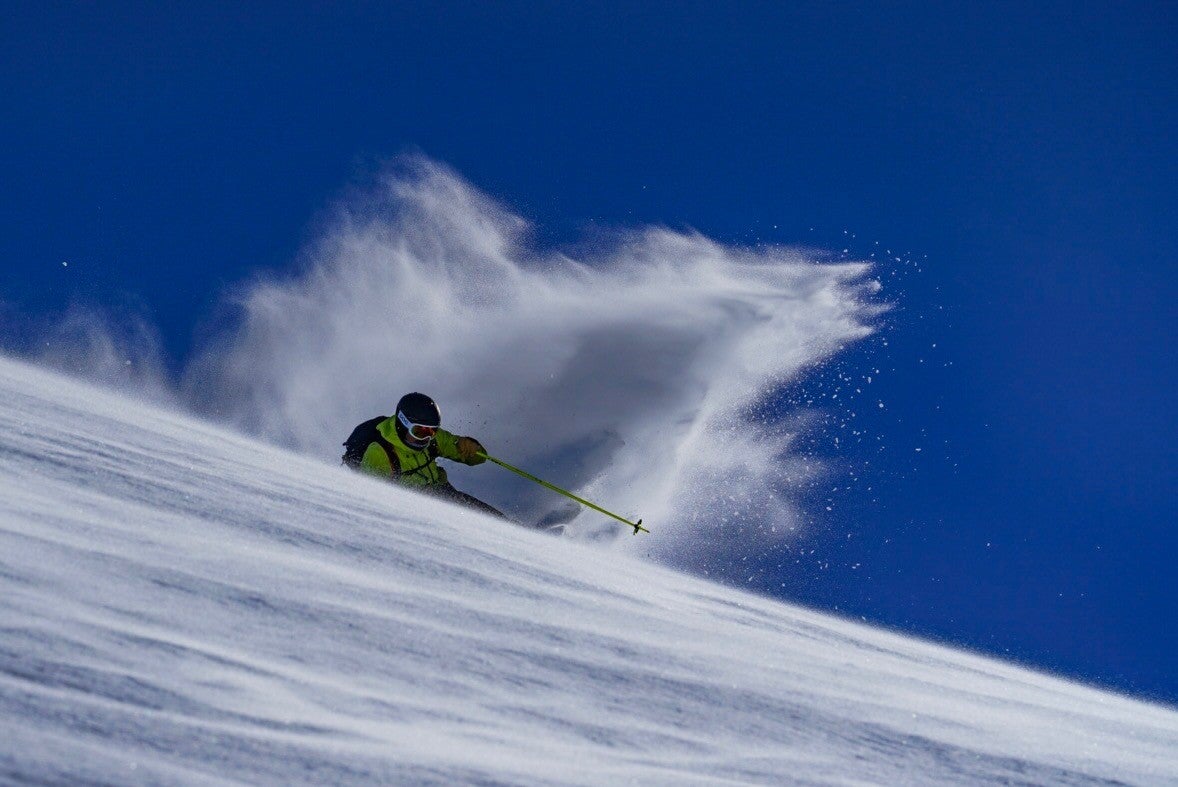 "Skier in bright green jacket skiing down slope in Swiss Alps"