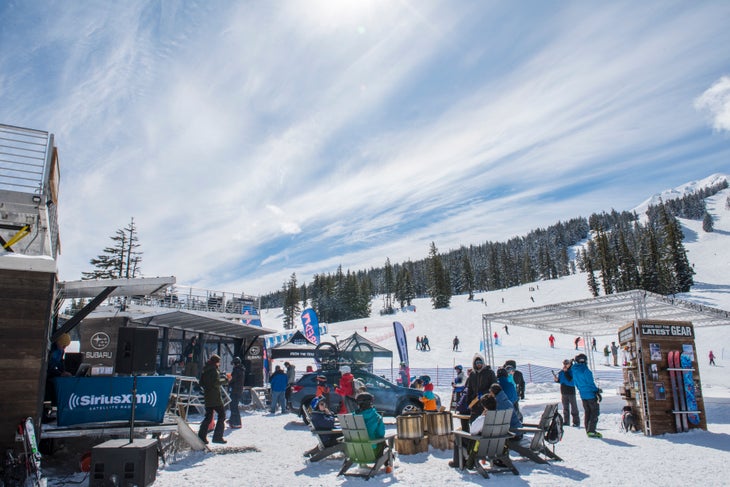 Bachelor031818_AB_009-web_Subaru Winterfest People sit in adirondack chairs at the base of Mt Bachelor on a sunny day. Stages and event tents surround them.