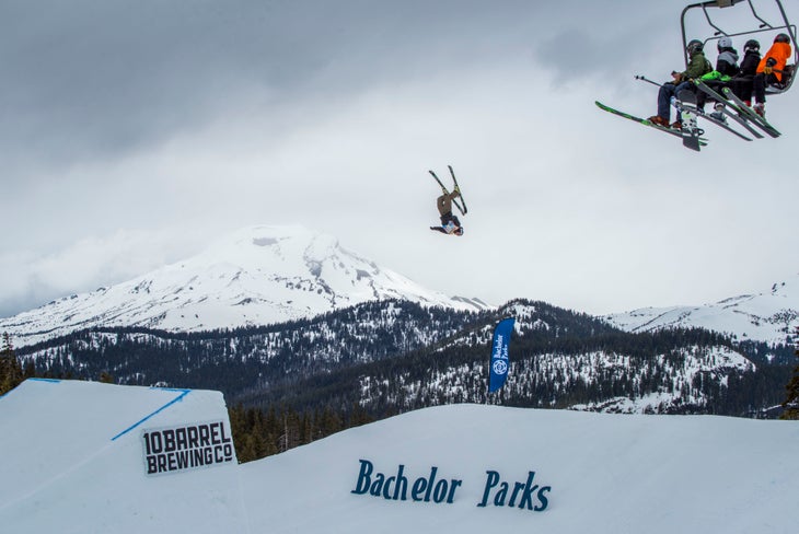 Bachelor033118_AB_066-web_HellaBigAir Four people sit on a chairlift and watch a person flipping off a ski jump.