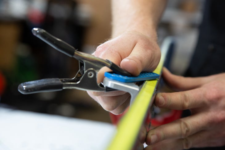 Technician sharpens ski side edge with diamond stone
