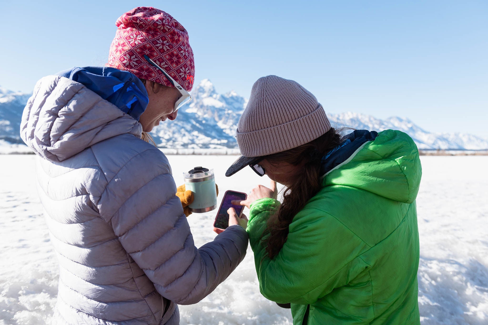 Two people looking at a phone with snow on the ground