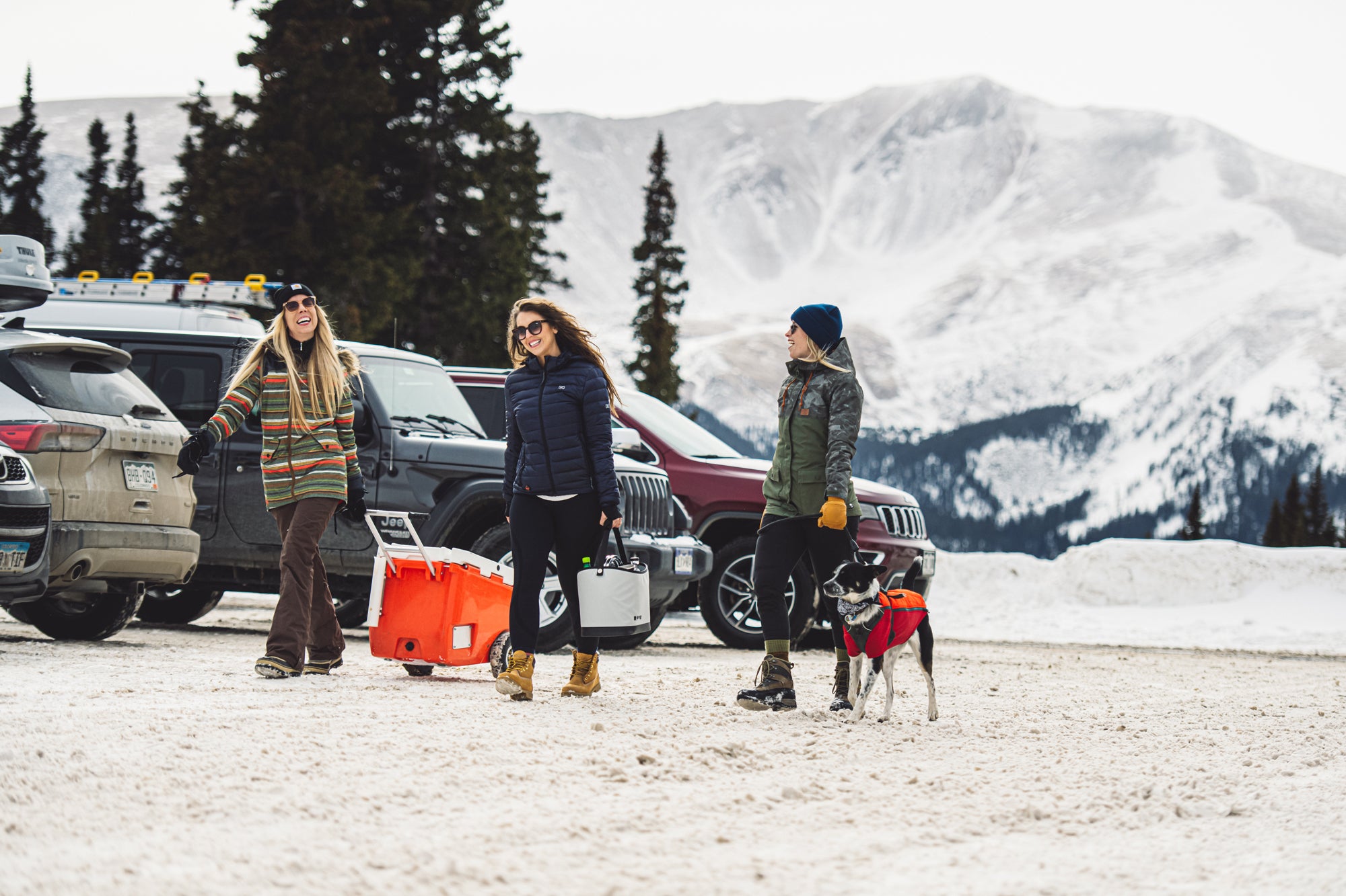 Three women in a snowy parking lot with a cooler