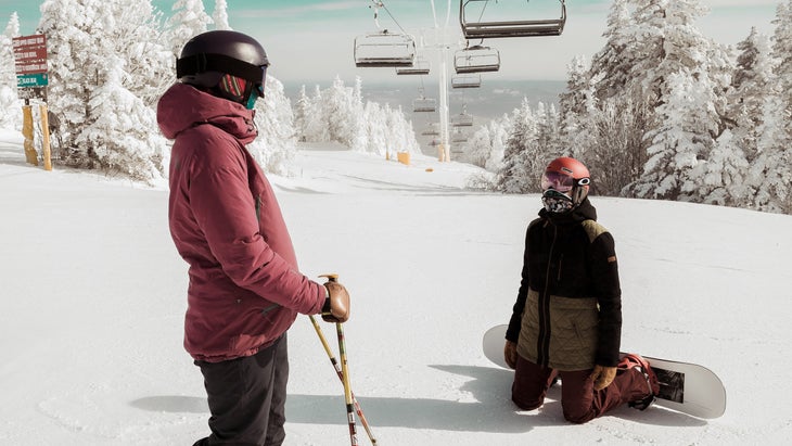 Skier and snowboarder under a chairlift.