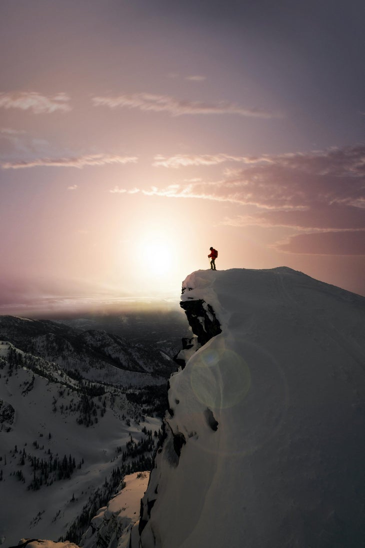Man standing on peak with sunset behind.