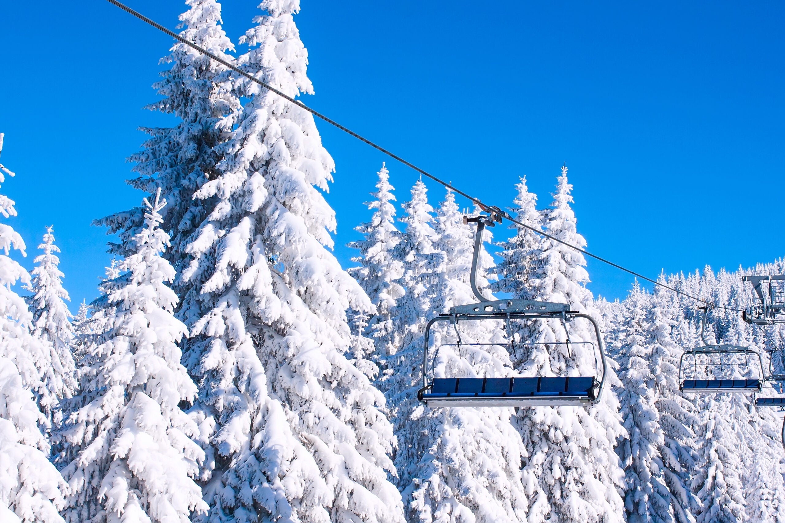 Ski resort image with empty chair lift, blue sky and white snowy pine trees at winter sunny day