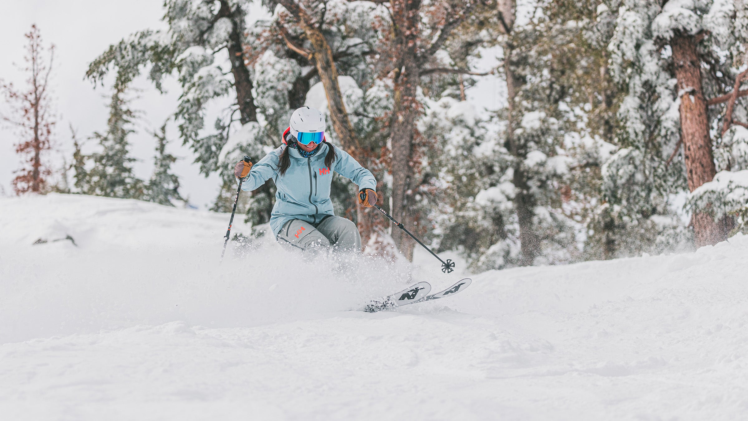 Woman in turquoise jacket skiing through soft snow on women's all-mountain skis at SKI Test